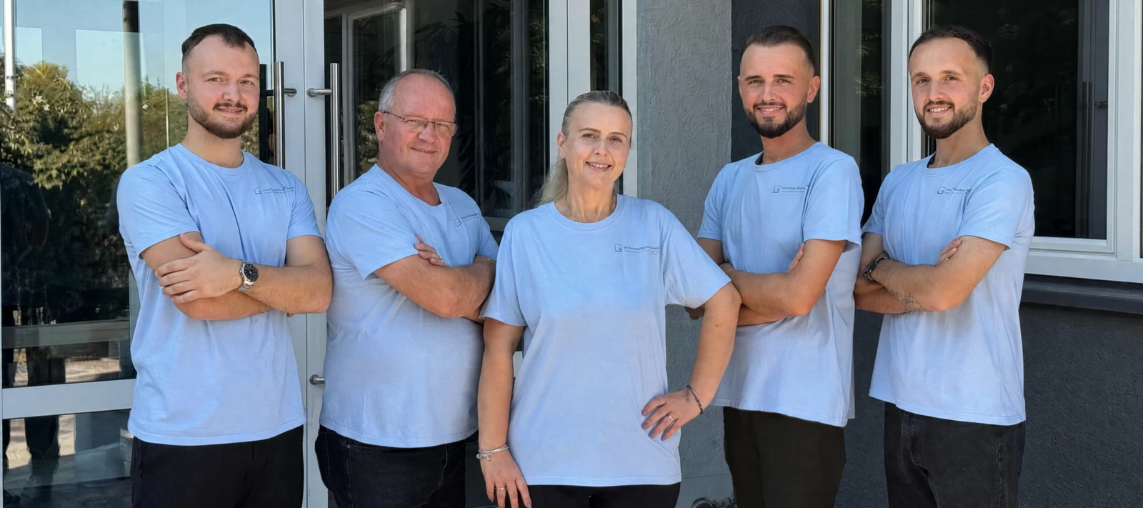 Die gesamte Familie Seferi: vier Männer und eine Frau in hellblauen Arbeits-Shirts vor einem Gebäudeeingang.